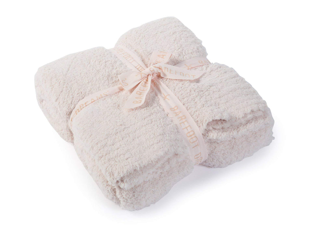 Barefoot Dreams plaid rose présenté sur un canapé, apportant confort décoratif