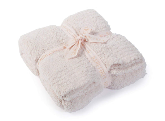 Barefoot Dreams plaid rose présenté sur un canapé, apportant confort décoratif